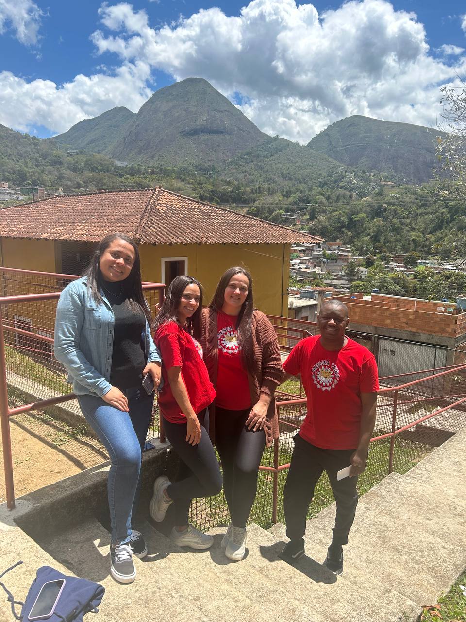 Equipe da Pequena Tribo reunida ao ar livre, com as montanhas de Petrópolis ao fundo.